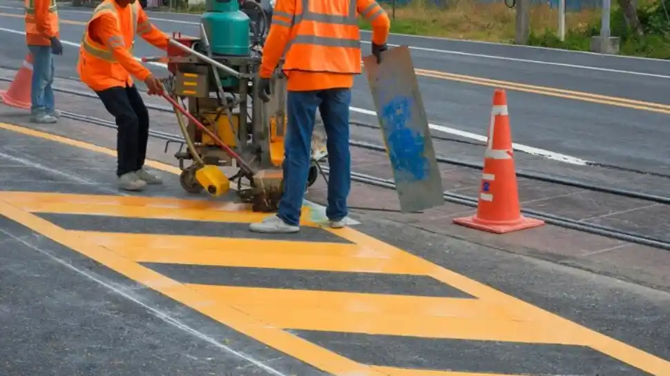 Road workers use a thermoplastic marking machine to paint yellow lines on the road