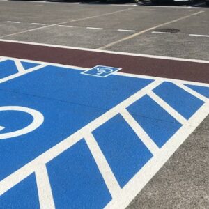 High-visibility accessible parking stencil markings in a parking lot with blue paint and white striping.