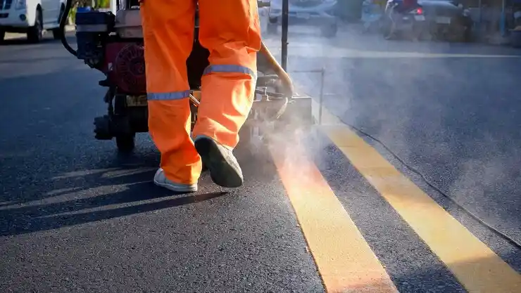 Worker applying roadway line markings on the asphalt surface in Ajax parking and traffic area.
